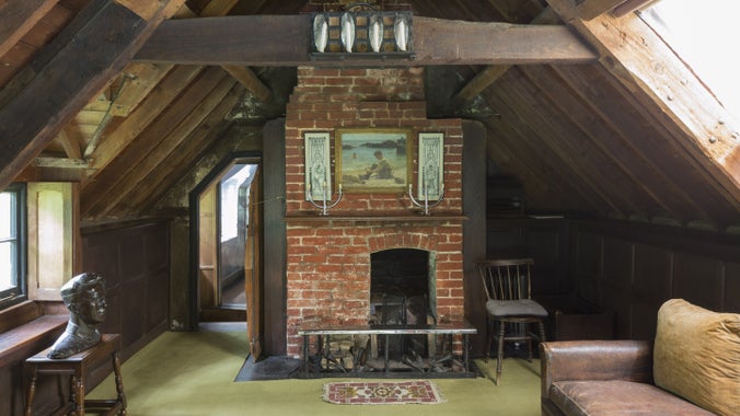 The upstairs living room at Clouds Hill, Dorset, which has exposed wooden beams, a brick fireplace and a brown leather sofa.